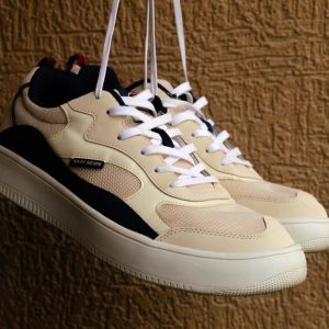 Stylish beige sneakers hanging against a textured wall, showcasing modern footwear design.